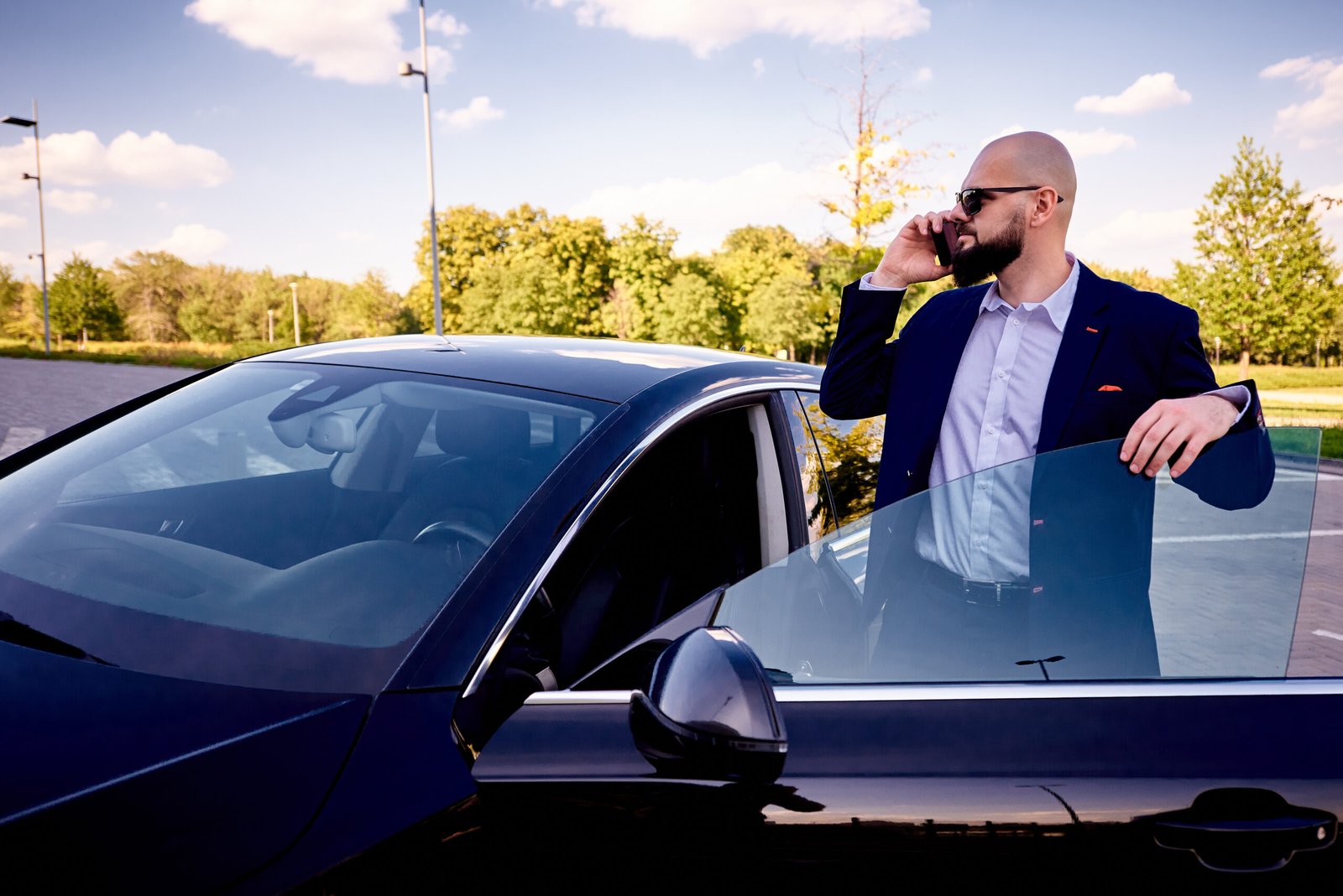 Successful young businessman with a smartphone near a auto in a parking lot.